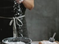 unrecognizable woman standing at table with various vegetables while making pasta dough in kitchen