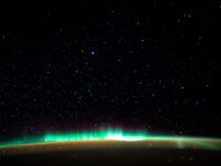 An aurora blankets the Earth beneath a celestial night sky