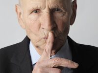 elderly gentleman making silence gesture in studio
